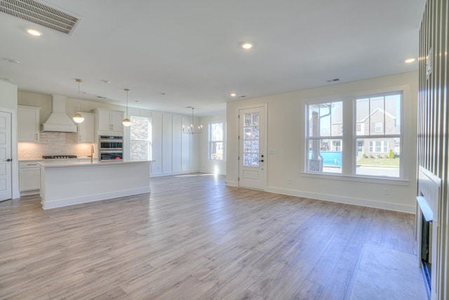 unfurnished living room with a notable chandelier, light wood-type flooring, sink, and a wealth of natural light