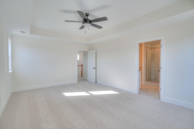 unfurnished bedroom featuring ensuite bath, light colored carpet, a raised ceiling, and ceiling fan