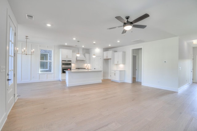 unfurnished living room with light hardwood / wood-style flooring, ceiling fan with notable chandelier, and sink