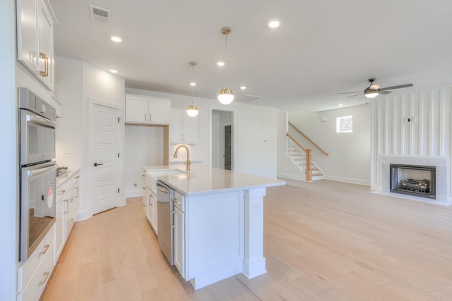 kitchen featuring a kitchen island with sink, sink, appliances with stainless steel finishes, decorative light fixtures, and white cabinetry