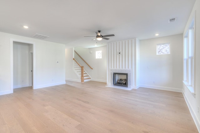 unfurnished living room featuring ceiling fan, a healthy amount of sunlight, a high end fireplace, and light hardwood / wood-style flooring