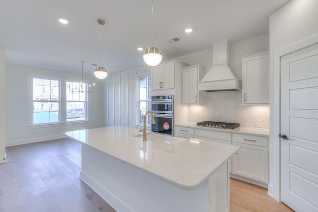 kitchen featuring white cabinetry, a center island with sink, appliances with stainless steel finishes, and custom exhaust hood