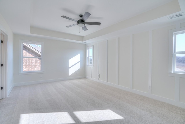 empty room with a tray ceiling, ceiling fan, and light colored carpet