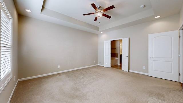 unfurnished bedroom with a tray ceiling, ceiling fan, and light carpet