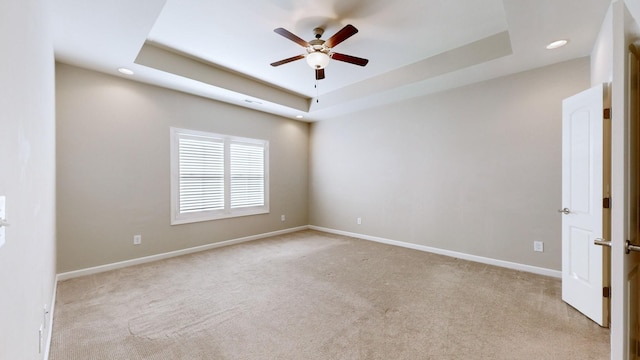 unfurnished room featuring ceiling fan, light colored carpet, and a tray ceiling