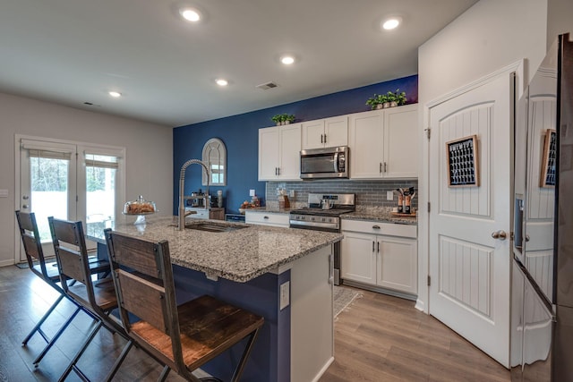 kitchen with white cabinetry, light stone countertops, sink, an island with sink, and appliances with stainless steel finishes