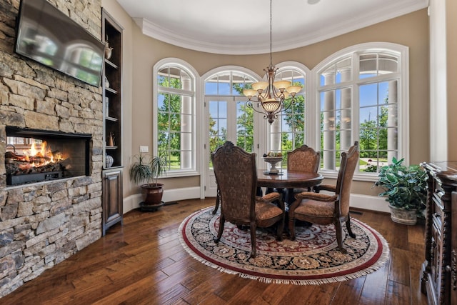 dining area featuring a stone fireplace, crown molding, built in features, dark hardwood / wood-style flooring, and a chandelier