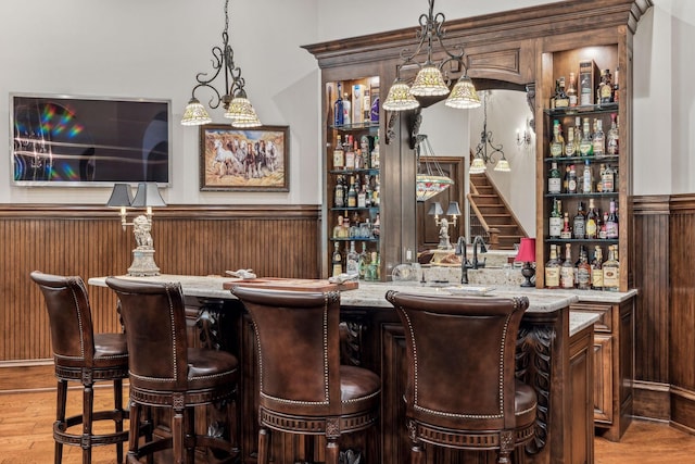 bar featuring wood walls, decorative light fixtures, and hardwood / wood-style flooring