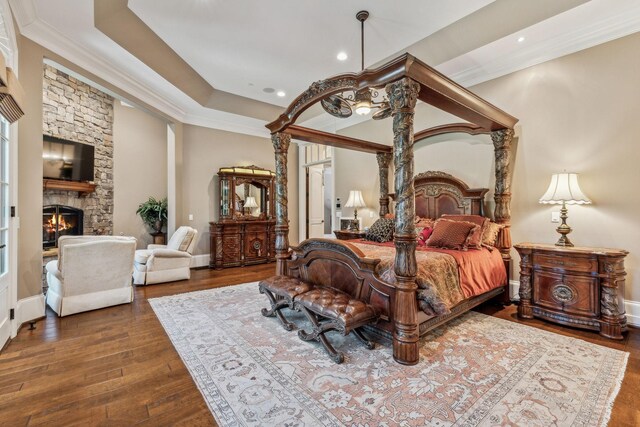 bedroom with dark hardwood / wood-style flooring, a stone fireplace, and ornamental molding