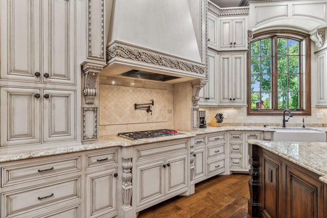 kitchen featuring backsplash, dark wood-type flooring, light stone countertops, custom range hood, and stainless steel gas cooktop