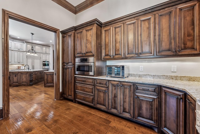 kitchen with light stone countertops, oven, pendant lighting, and ornamental molding