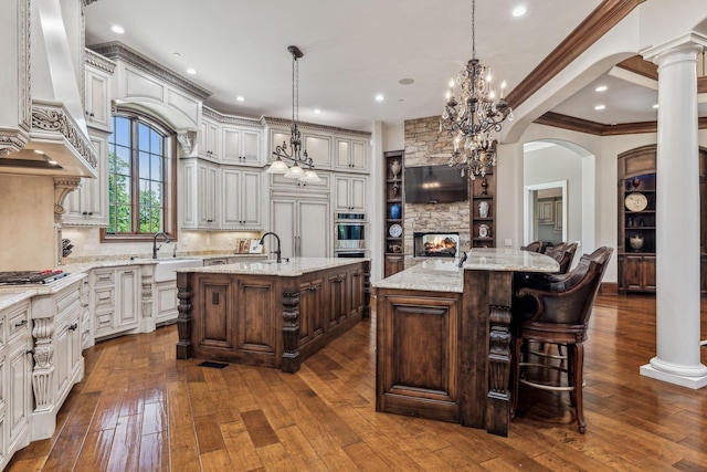 kitchen with tasteful backsplash, light stone counters, custom range hood, pendant lighting, and a center island with sink