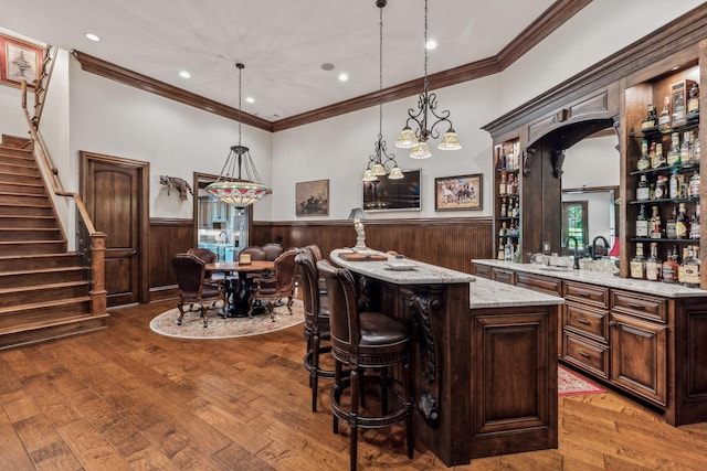 bar with hardwood / wood-style floors, hanging light fixtures, ornamental molding, dark brown cabinets, and light stone counters