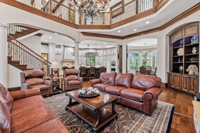 living room with a notable chandelier, dark hardwood / wood-style floors, ornate columns, and a high ceiling