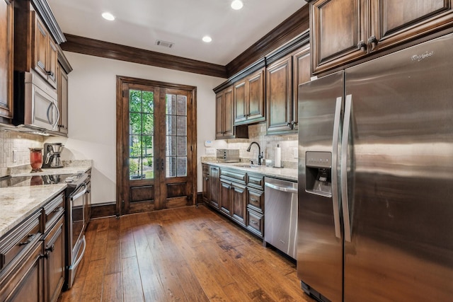 kitchen featuring dark wood-type flooring, sink, decorative backsplash, light stone countertops, and appliances with stainless steel finishes