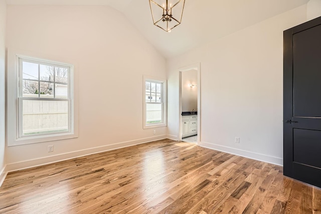 unfurnished bedroom featuring light wood-type flooring, connected bathroom, multiple windows, and a notable chandelier