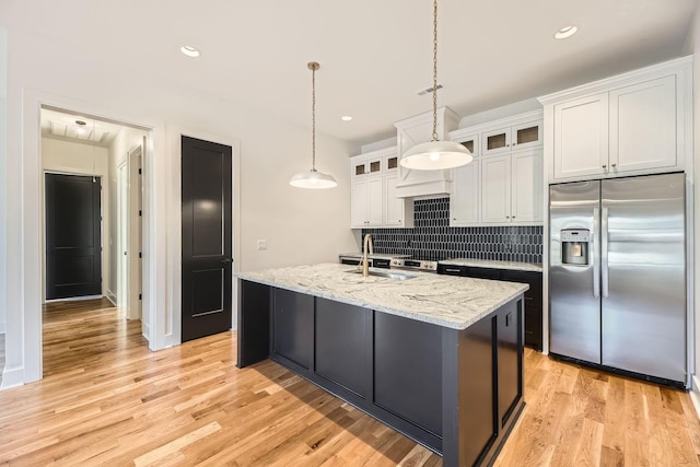 kitchen featuring sink, white cabinets, stainless steel fridge with ice dispenser, light hardwood / wood-style floors, and an island with sink