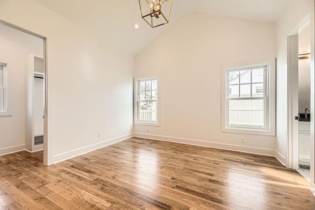 unfurnished bedroom featuring multiple windows, an inviting chandelier, lofted ceiling, and hardwood / wood-style flooring