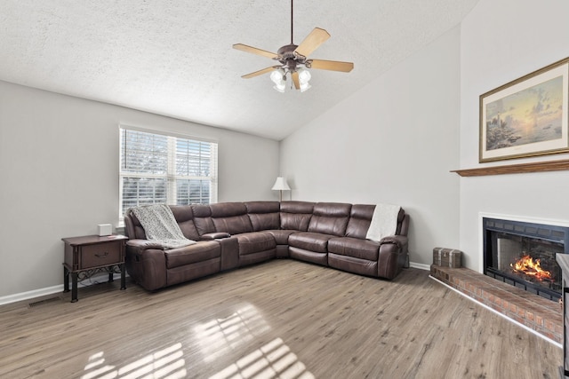 living room featuring lofted ceiling, ceiling fan, light wood-type flooring, a fireplace, and a textured ceiling