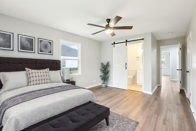 bedroom with hardwood / wood-style floors, a barn door, ensuite bathroom, and ceiling fan