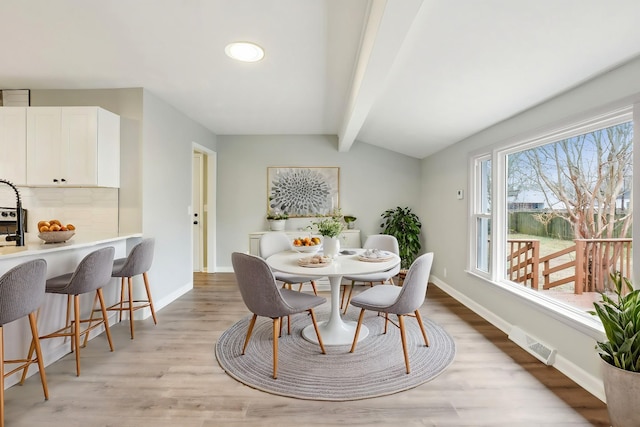 dining space featuring lofted ceiling with beams and light hardwood / wood-style flooring