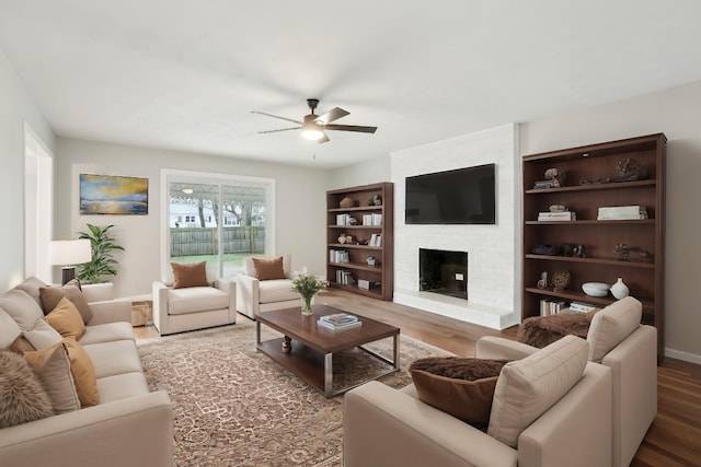 living area with a brick fireplace, ceiling fan, baseboards, and wood finished floors