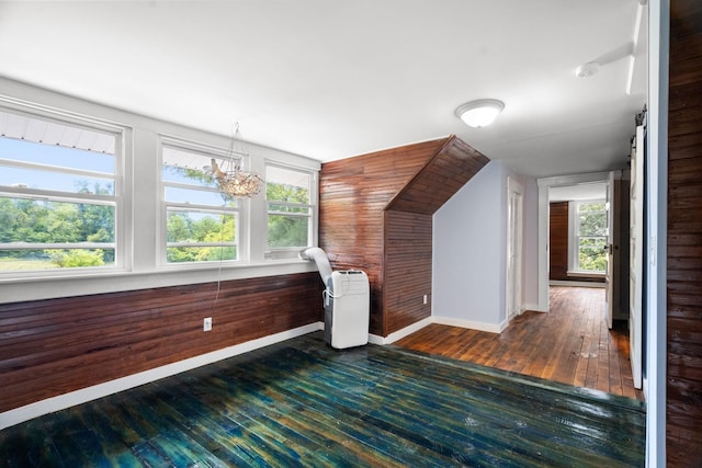 bonus room featuring an inviting chandelier, a healthy amount of sunlight, and wood walls