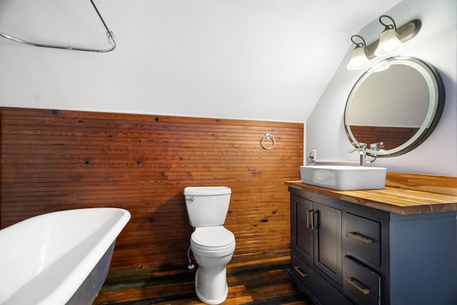 bathroom with a tub to relax in, wood-type flooring, vaulted ceiling, toilet, and vanity