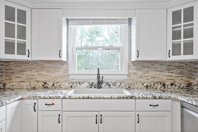 kitchen with light stone counters, white cabinetry, and sink