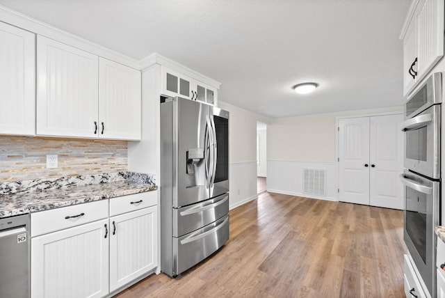 kitchen featuring white cabinetry, stainless steel appliances, light stone counters, decorative backsplash, and light wood-type flooring