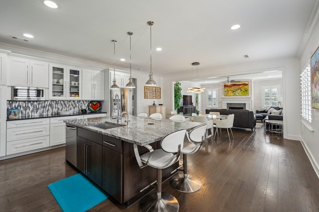 kitchen with light stone countertops, white cabinetry, sink, stainless steel appliances, and an island with sink