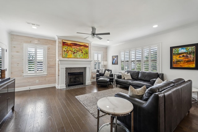 living room featuring dark wood-type flooring, crown molding, wooden walls, ceiling fan, and a fireplace