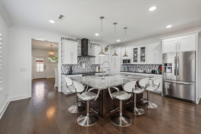 kitchen with white cabinetry, sink, hanging light fixtures, wall chimney range hood, and appliances with stainless steel finishes