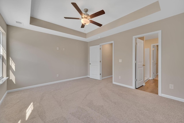 unfurnished bedroom featuring ceiling fan, a raised ceiling, and light colored carpet