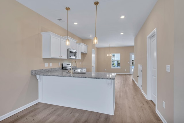 kitchen with sink, stainless steel appliances, kitchen peninsula, pendant lighting, and white cabinets