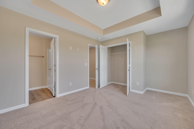 unfurnished bedroom with light carpet, a raised ceiling, and a closet