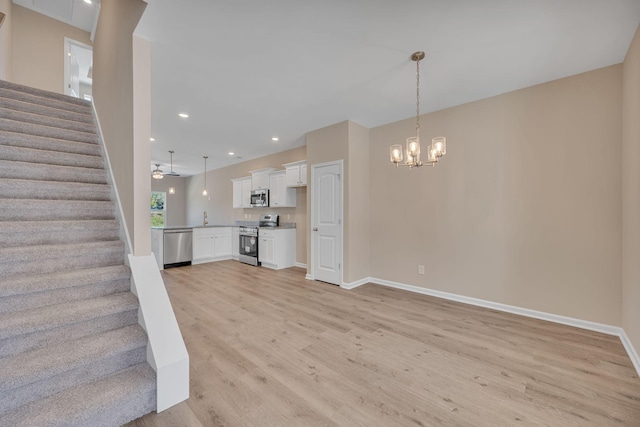 unfurnished living room with ceiling fan with notable chandelier and light hardwood / wood-style floors