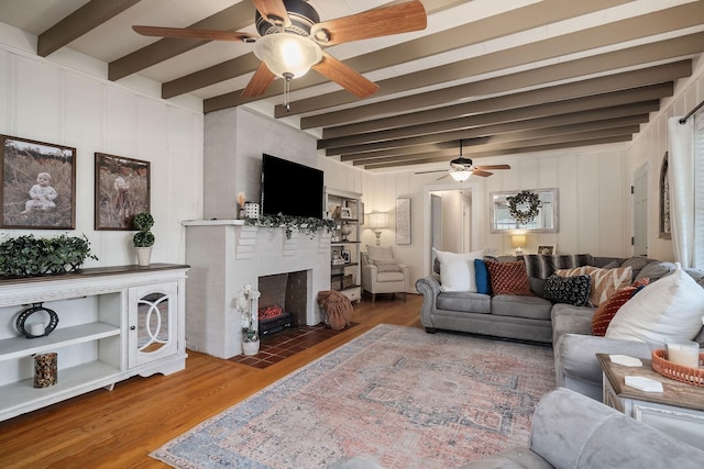 living room featuring beamed ceiling, hardwood / wood-style floors, and a brick fireplace