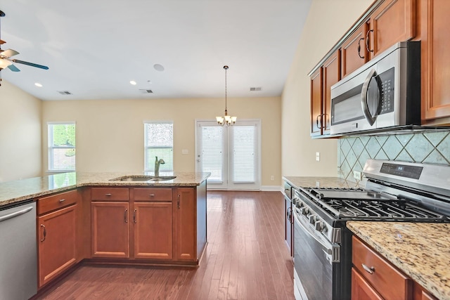 kitchen featuring sink, dark hardwood / wood-style floors, appliances with stainless steel finishes, decorative light fixtures, and light stone counters