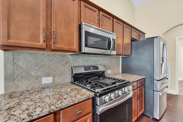 kitchen with light stone countertops, dark hardwood / wood-style flooring, stainless steel appliances, and tasteful backsplash