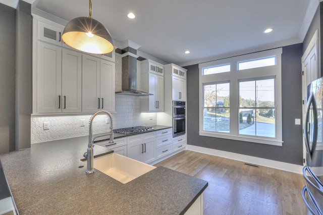 kitchen featuring white cabinetry, sink, stainless steel appliances, wall chimney range hood, and pendant lighting