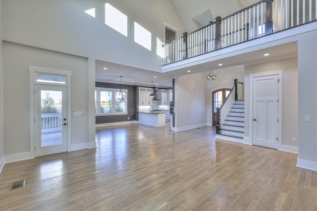 unfurnished living room with a high ceiling, light hardwood / wood-style floors, and a notable chandelier