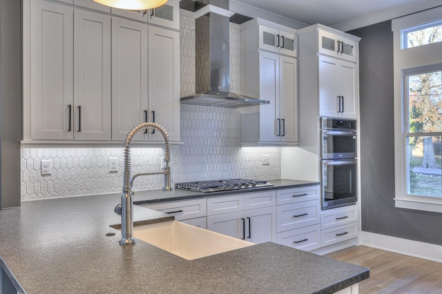 kitchen with sink, light hardwood / wood-style flooring, wall chimney exhaust hood, white cabinetry, and stainless steel appliances