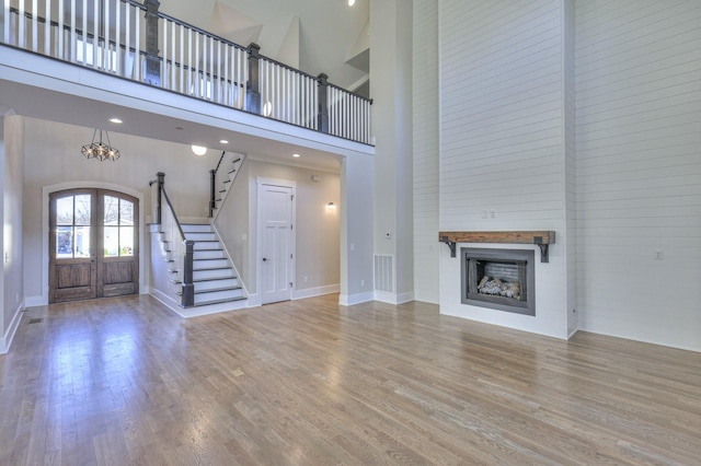 unfurnished living room with french doors, a towering ceiling, a notable chandelier, and wood-type flooring