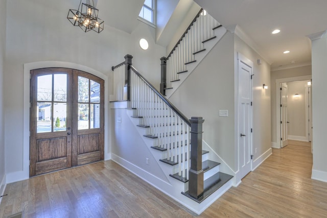 entryway with a chandelier, french doors, light hardwood / wood-style floors, and crown molding