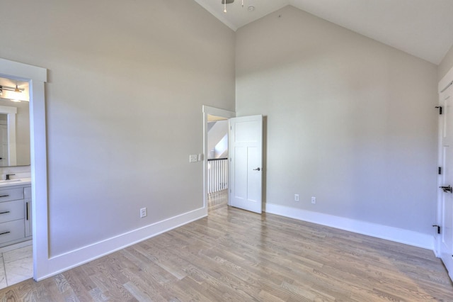 unfurnished bedroom featuring ensuite bathroom, sink, high vaulted ceiling, and light wood-type flooring