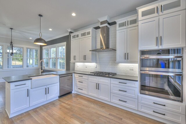 kitchen with pendant lighting, stainless steel appliances, white cabinetry, and wall chimney exhaust hood