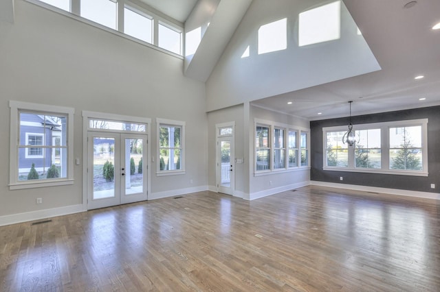 unfurnished living room featuring french doors, wood-type flooring, a healthy amount of sunlight, and an inviting chandelier