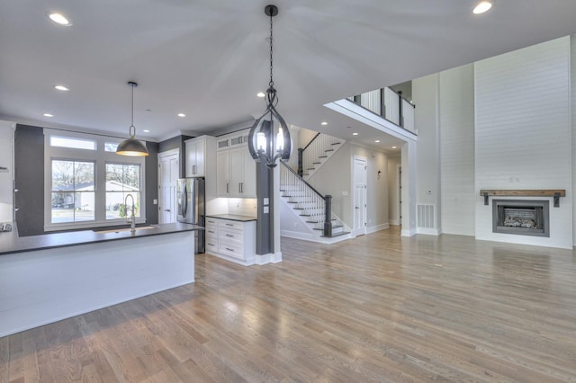 kitchen with white cabinetry, sink, stainless steel fridge with ice dispenser, decorative light fixtures, and light wood-type flooring