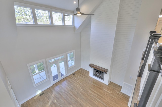 unfurnished living room with ceiling fan, light wood-type flooring, a high ceiling, and french doors